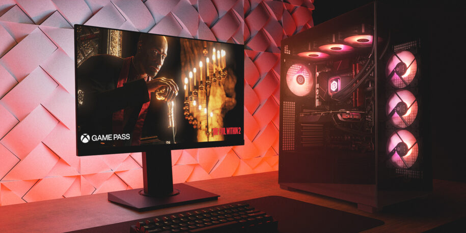 A gaming PC, monitor, and keyboard on a wooden desk in a dark room with moody red lighting.