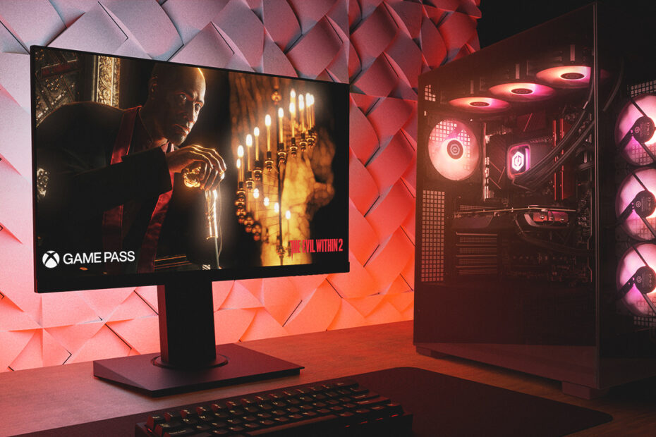 A gaming PC, monitor, and keyboard on a wooden desk in a dark room with moody red lighting.