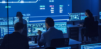 Modern control room with people at computers and blue-lit screens showing complex data.